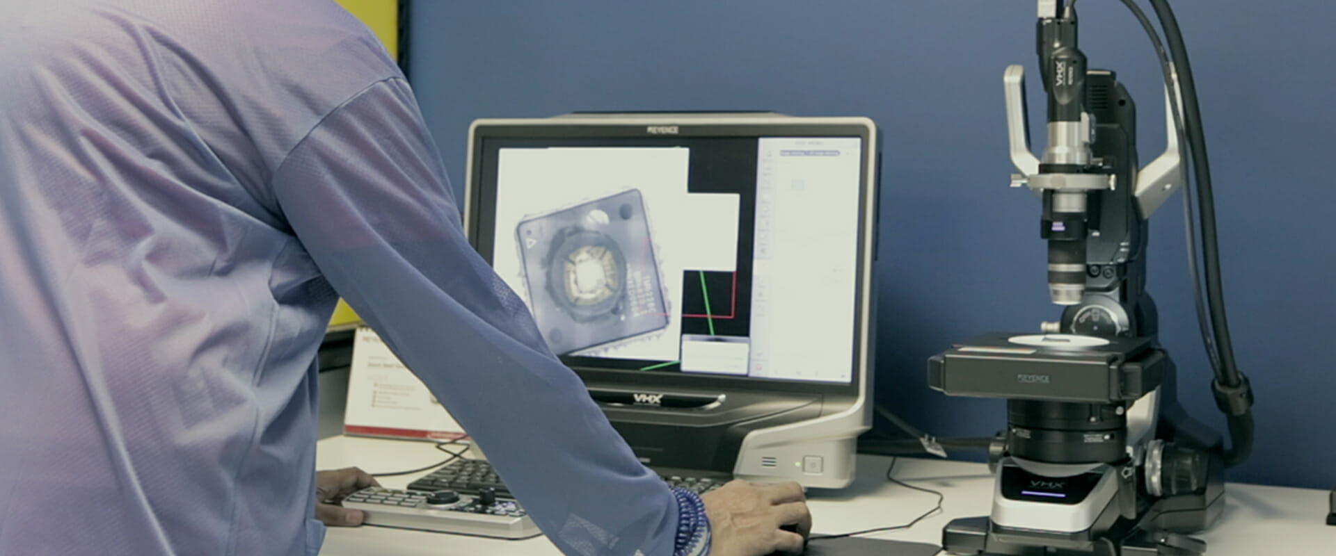 A person in a lab coat analyzes the sourceability of microscopic data on a computer screen next to a microscope.