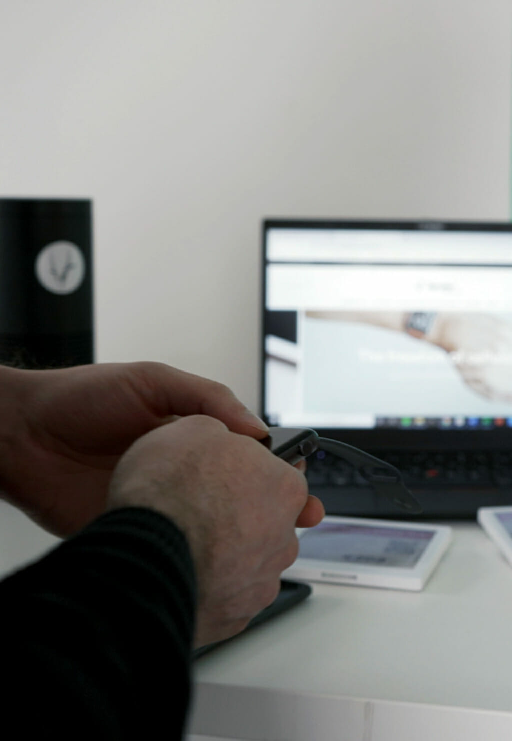 Two people working at a desk. One holds a card showing €145.99, while the other handles a small item. A laptop in the background displays the emerce 100 website.