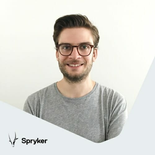 A man with glasses and a beard, wearing a gray shirt, smiles at the camera. The image includes the logo and text "Spryker" in the bottom left corner, highlighting its innovative retail booster capabilities.