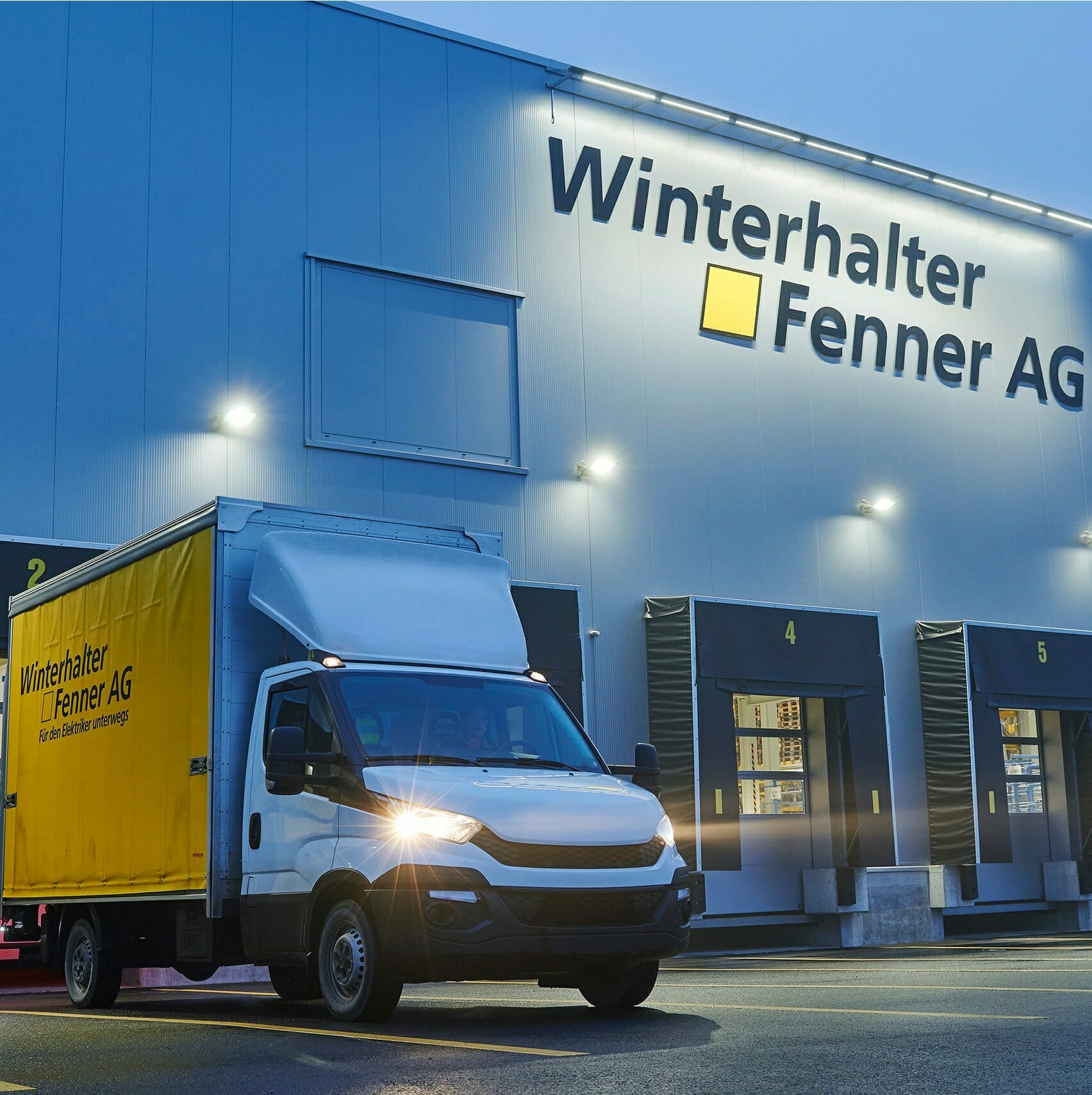 A delivery truck parked outside the Winterhalter+Fenner AG building, proudly displaying the company's name and logo on its side and on the building facade. Several loading docks are visible.