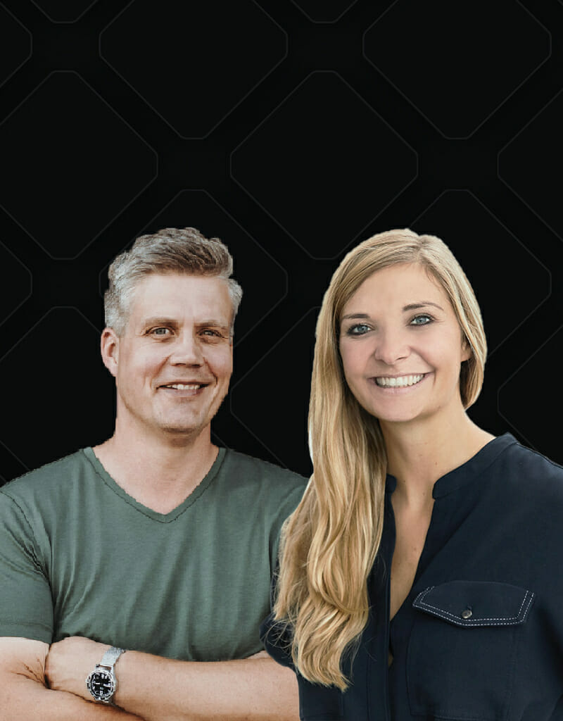 A man in a green shirt and a woman in a black shirt stand side by side, smiling, against a dark, patterned background, reminiscent of the vibrant energy at a powwow.