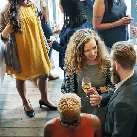 Group of people socializing at an indoor gathering, casually conversing and holding drinks, reminiscent of the engaging atmosphere at a HERd Conference.