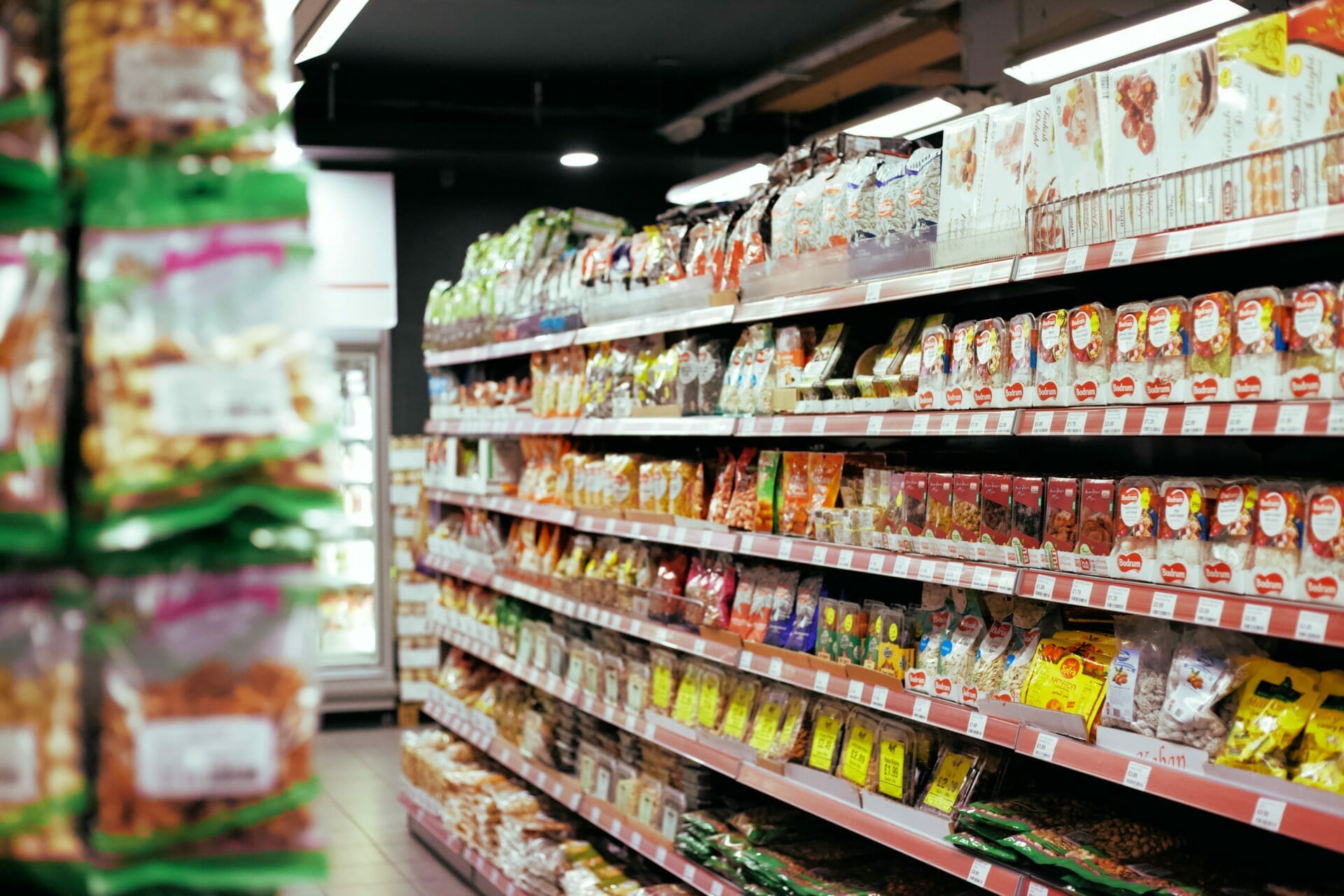 A grocery store aisle resembles a mini makro, filled with various packaged food items and shelves stocked from top to bottom.