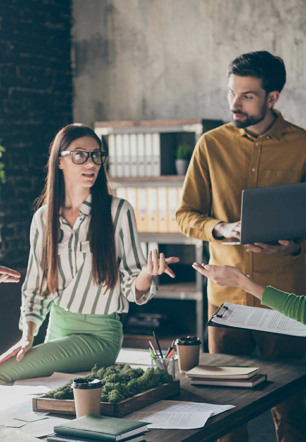 A group of four individuals engaged in a discussion in an office setting, with Tom Reiter and another person holding a laptop and a clipboard. Shelves with folders are visible in the background, creating a professional atmosphere perfect for Spryker OnAir insights.