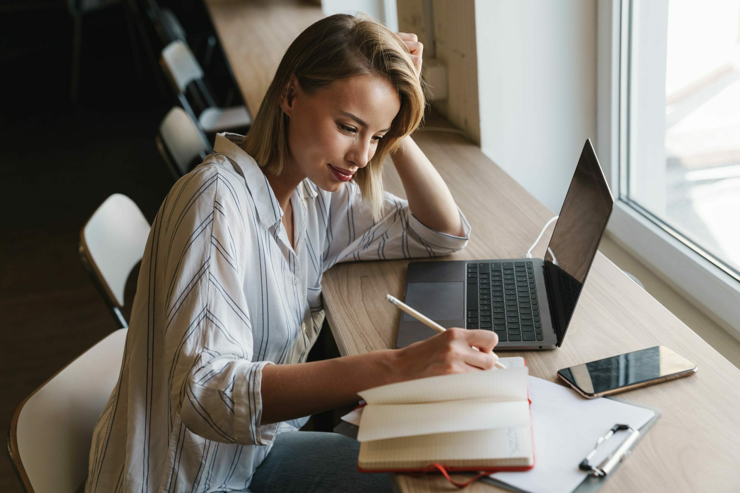 Woman with macbook writing on a notebook