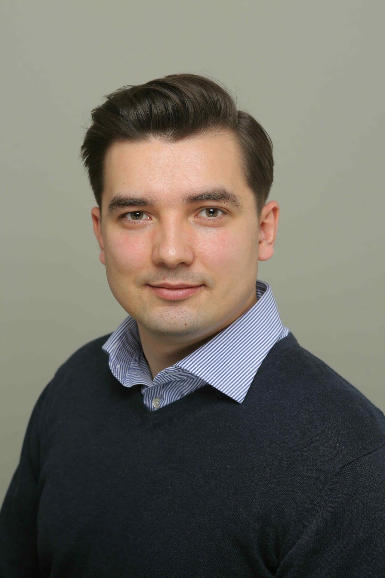 A man with short dark hair, wearing a dark sweater over a blue collared shirt, poses against a neutral background, embodying the sophistication of Packaged Business Capabilities.