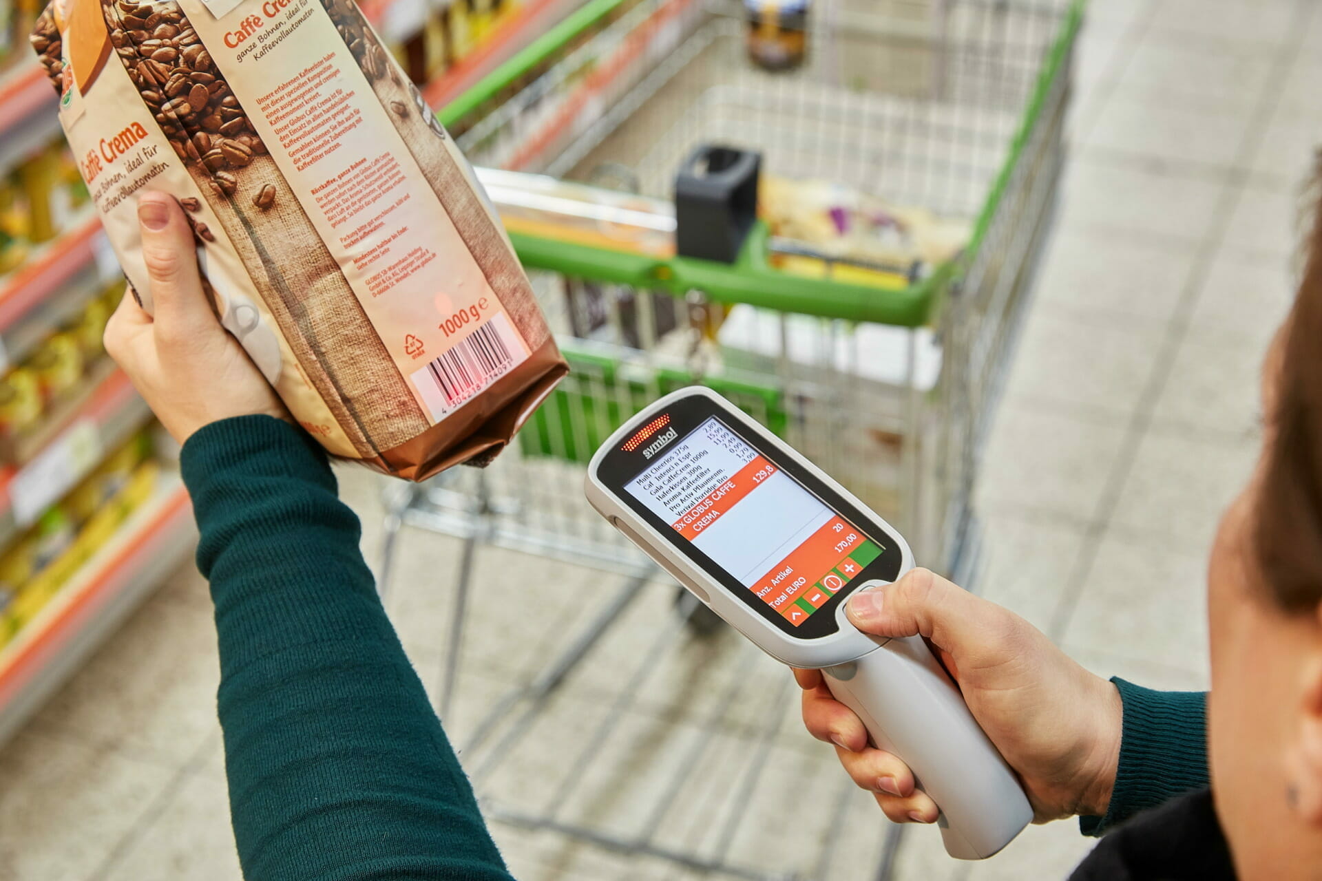 Person scanning a bag of Globus coffee beans with a handheld barcode scanner in a supermarket aisle, with a shopping cart in the background.