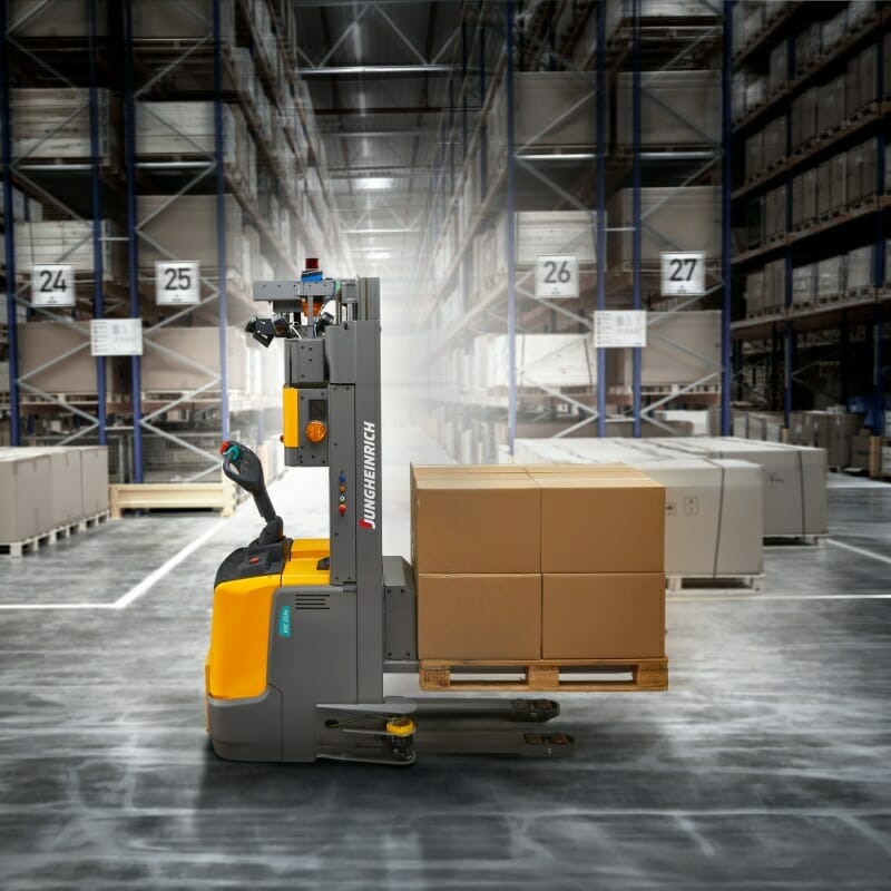 A Spryker automated guided vehicle effortlessly transports a pallet of boxes through a large warehouse with tall shelves and organized aisles.