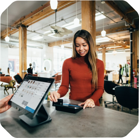 A woman in a red sweater uses a card reader to make a payment at a counter in a well-lit, modern space with wooden beams, hinting at recent expansion. A digital point of sale system is visible.