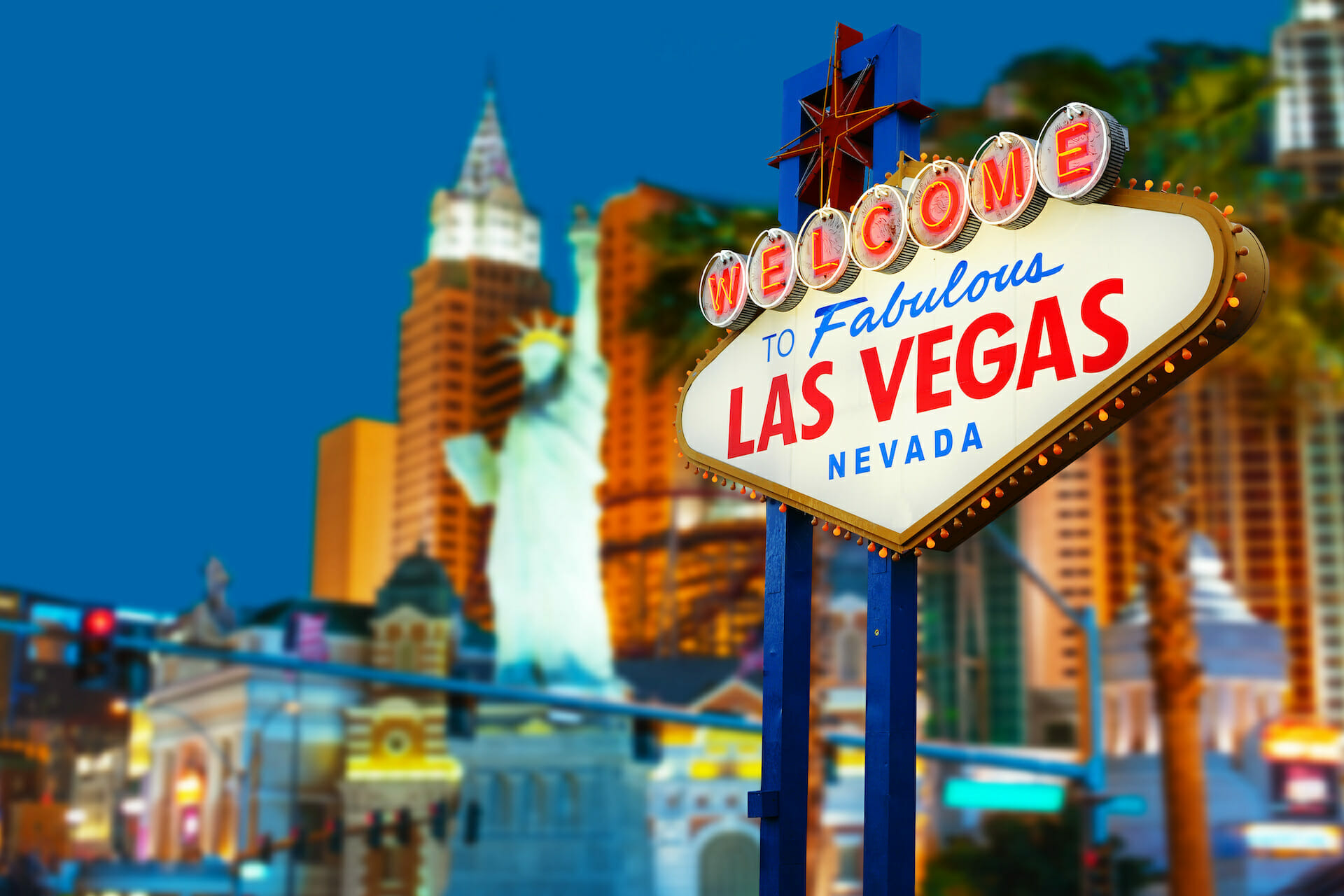 A lit-up "Welcome to Fabulous Las Vegas, Nevada" sign is in the foreground with various brightly lit buildings and a Statue of Liberty replica in the background at night, setting the stage for Shoptalk Las Vegas 2023.