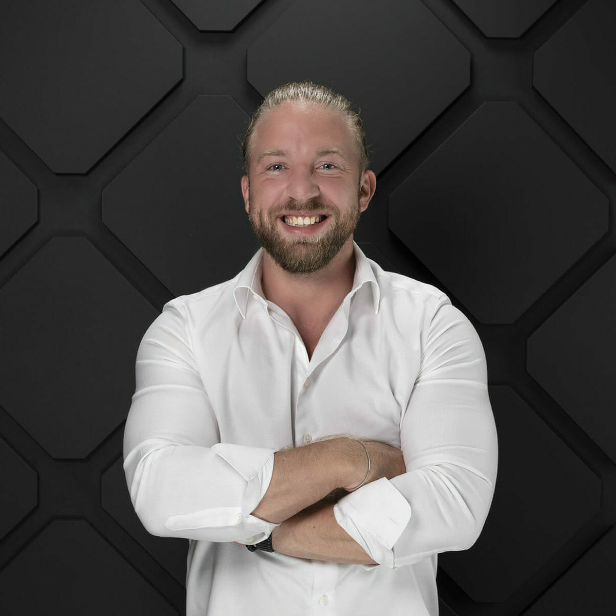 A person with long hair tied back, wearing a white dress shirt, stands with arms crossed in front of a dark geometric background, exuding an air of digital success.