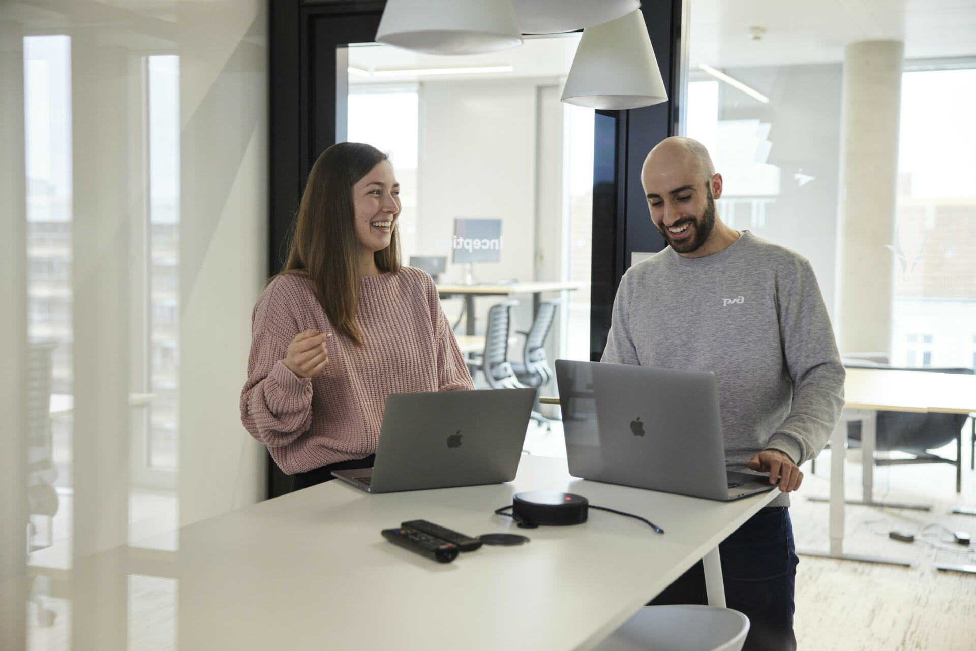 Two people stand at a high table in the Trevipay office, each with a laptop. They are smiling and engaged in conversation.