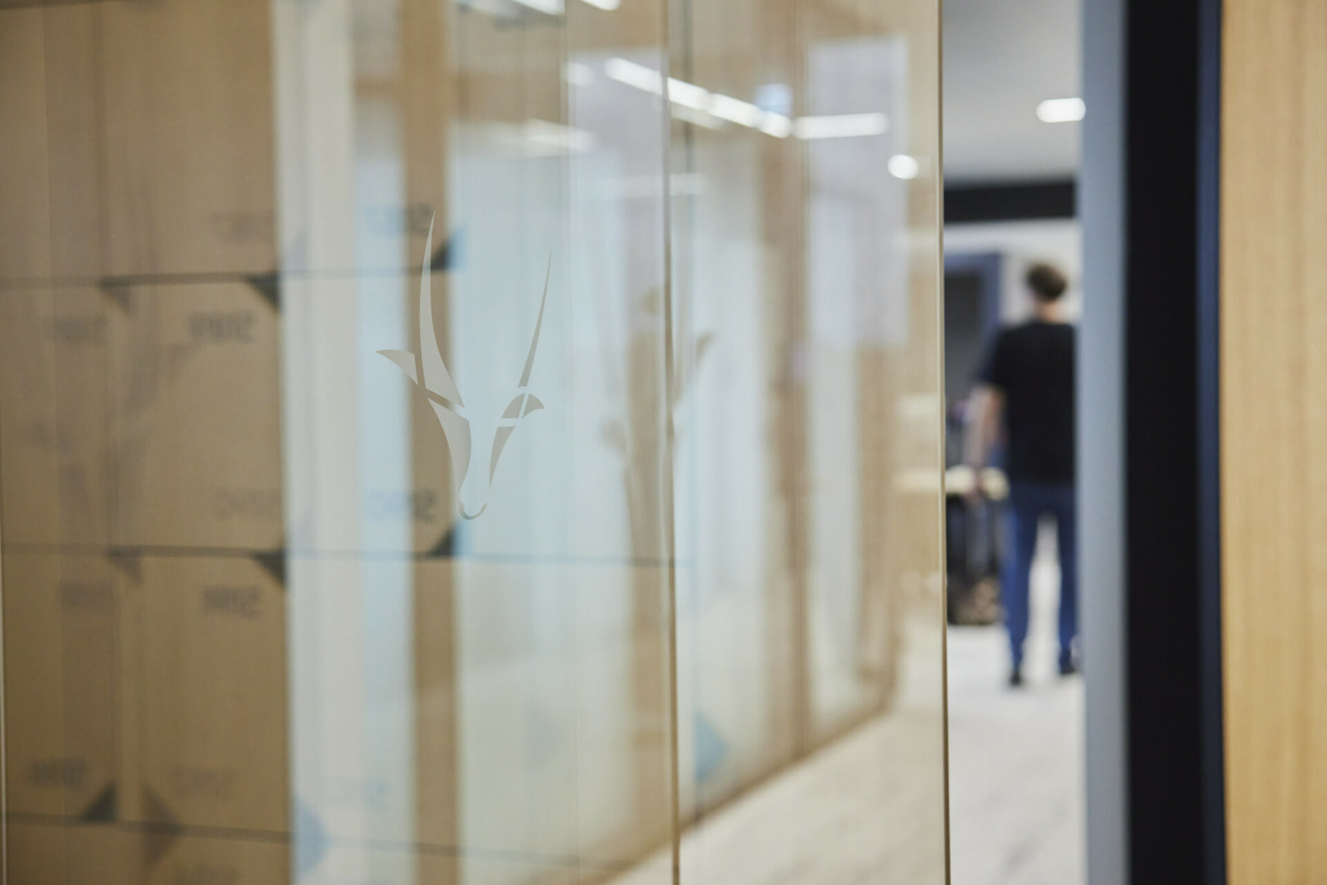 Frosted glass panel with an antelope logo in an office hallway; a person is blurred in the background, adding a touch of modern professionalism to the Trevipay headquarters.