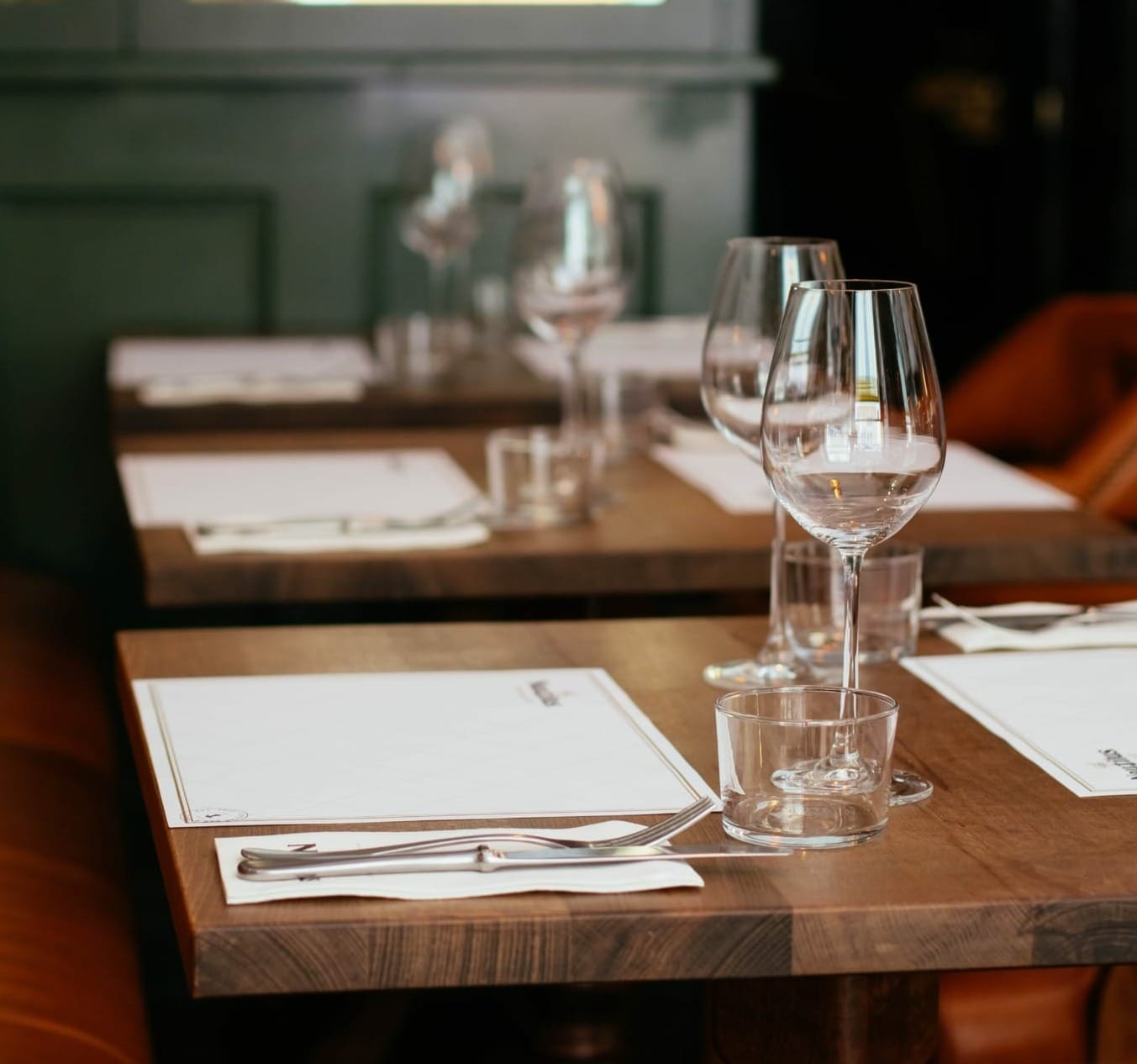 A neatly set wooden dining table with white placemats, empty wine glasses, water glasses, and cutlery in a restaurant, commonly visited by B2B Online Europe manufacturers and distributors for business lunches.