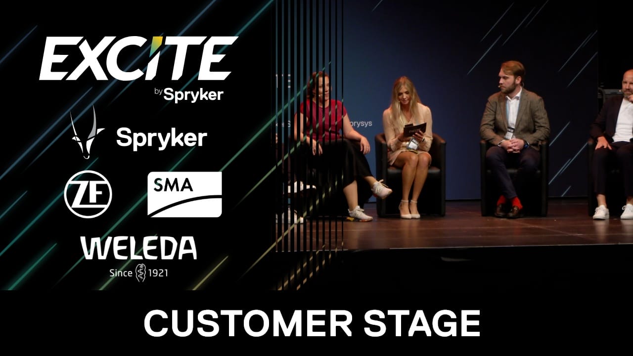 A panel of four people sitting on stage at the Excite by Spryker event discusses digital commerce trends. The backdrop features logos for Spryker, ZF, SMA, and Weleda, with "CUSTOMER STAGE" displayed at the bottom.