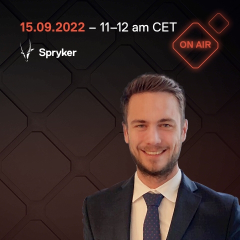 Man in a suit smiling in front of a background with dates, times, and logos including "Spryker" and "Onair.