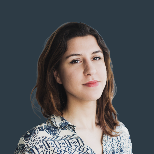A person with long brown hair and a patterned shirt stands against a dark blue background, looking slightly to the side with a neutral expression, embodying the poised professionalism often associated with cloud commerce.